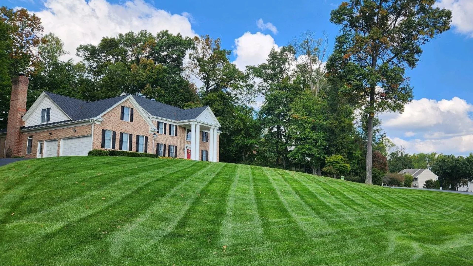 Expansive green lawn on a hill with a house in the background under a clear sky